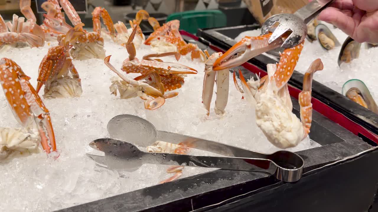 Hand uses tongs to serve sand crab claw onto plate from chilled seafood buffet display