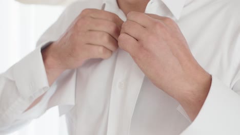 close-up of a groom buttoning his white shirt in preparation for the wedding