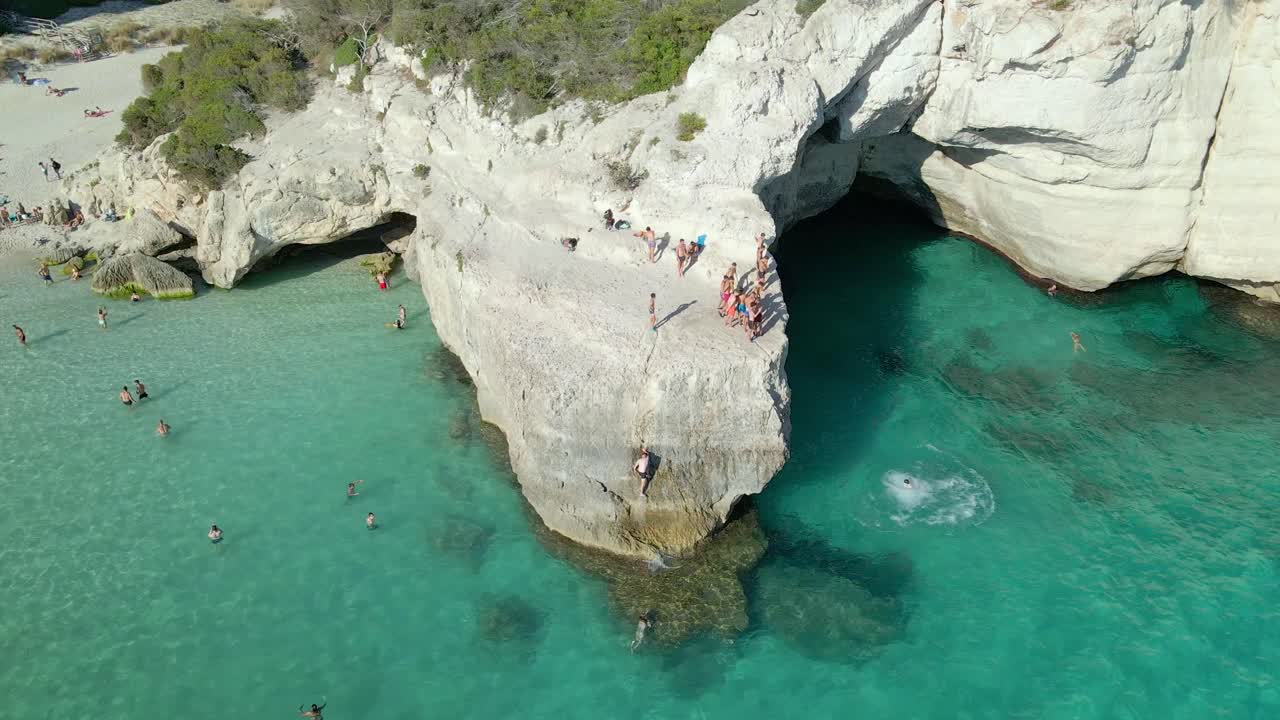 Group of kids cliff jumping on rock in Cala Mitjana, Spain