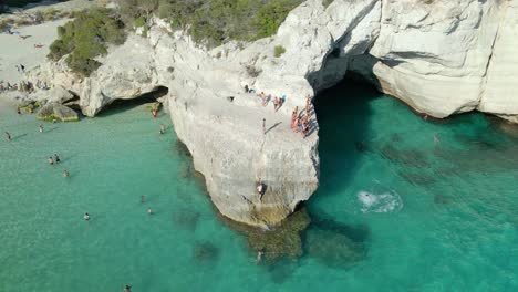 group of kids cliff jumping on rock in cala mitjana, spain