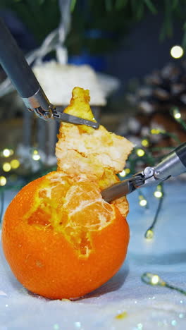 high-tech equipment peeling mandarin. metal cybernetic tools on christmas decorations background. futuristic innovations. vertical video
