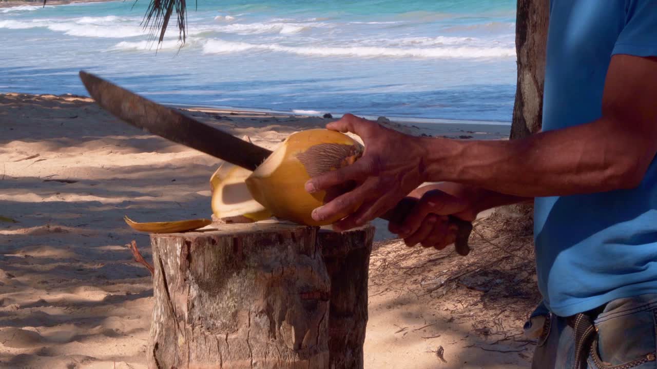 hombre corta coco del agua para ofrecer a los turistas en una playa tropical