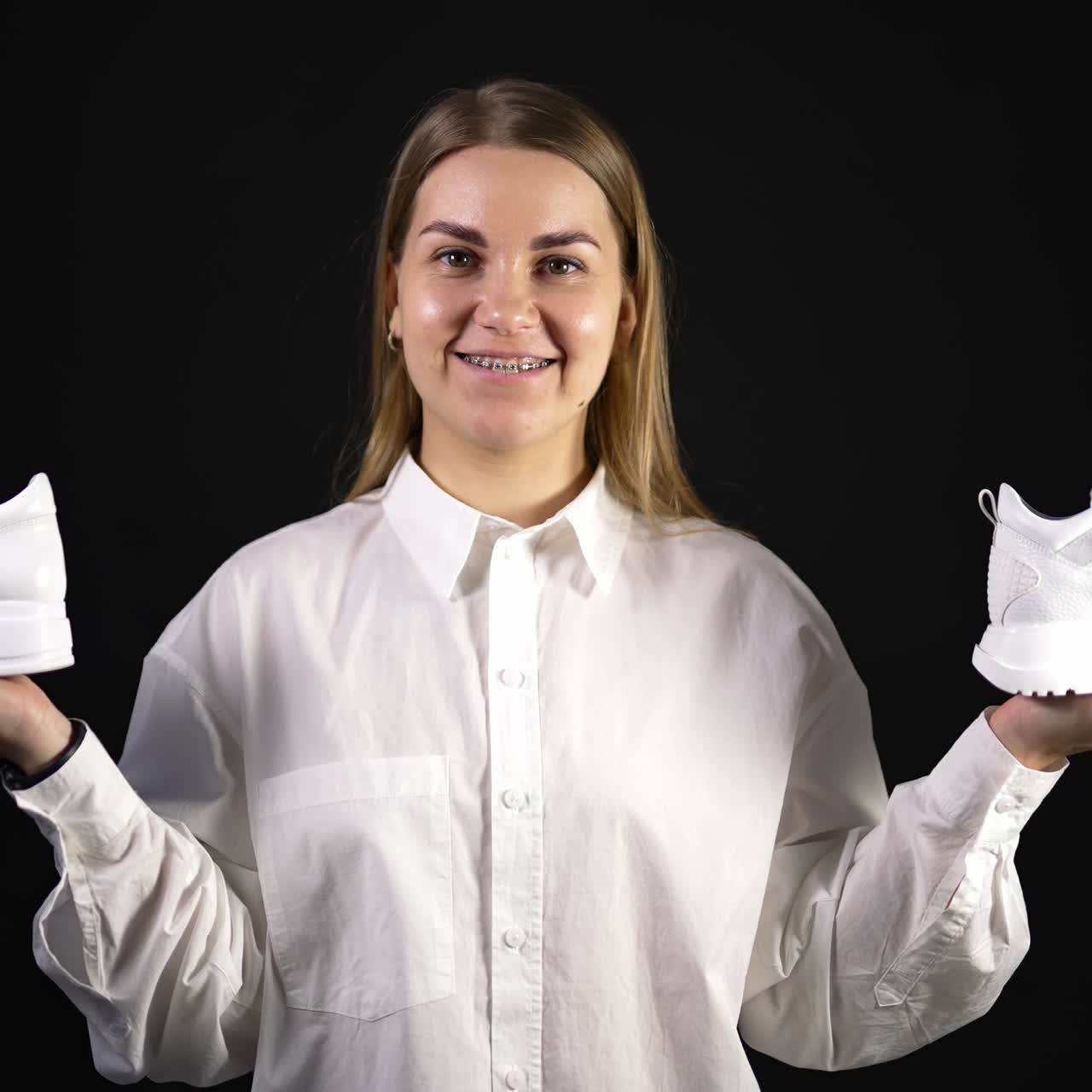 Giovane donna che tiene in mano un paio di sneakers bianche nuove. Bellissimo paio di scarpe sportive nuove su sfondo nero