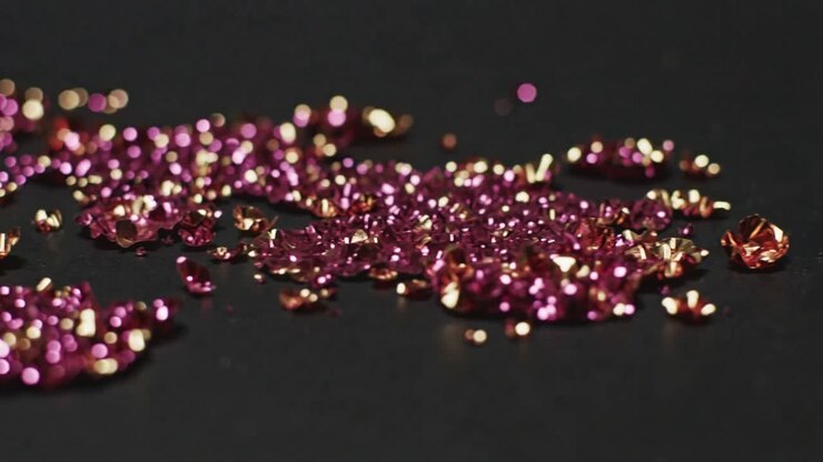 Regolazione della messa a fuoco, obiettivo macro che inquadra un tavolo in studio, rivelando gemme rosa tagliate e coppe d'oro per brillantezza