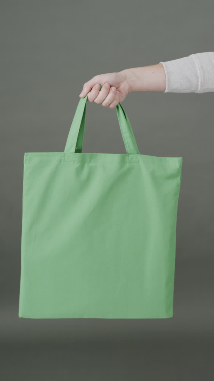 Vertical video of hand of caucasian woman with green canvas bag and copy space on grey background