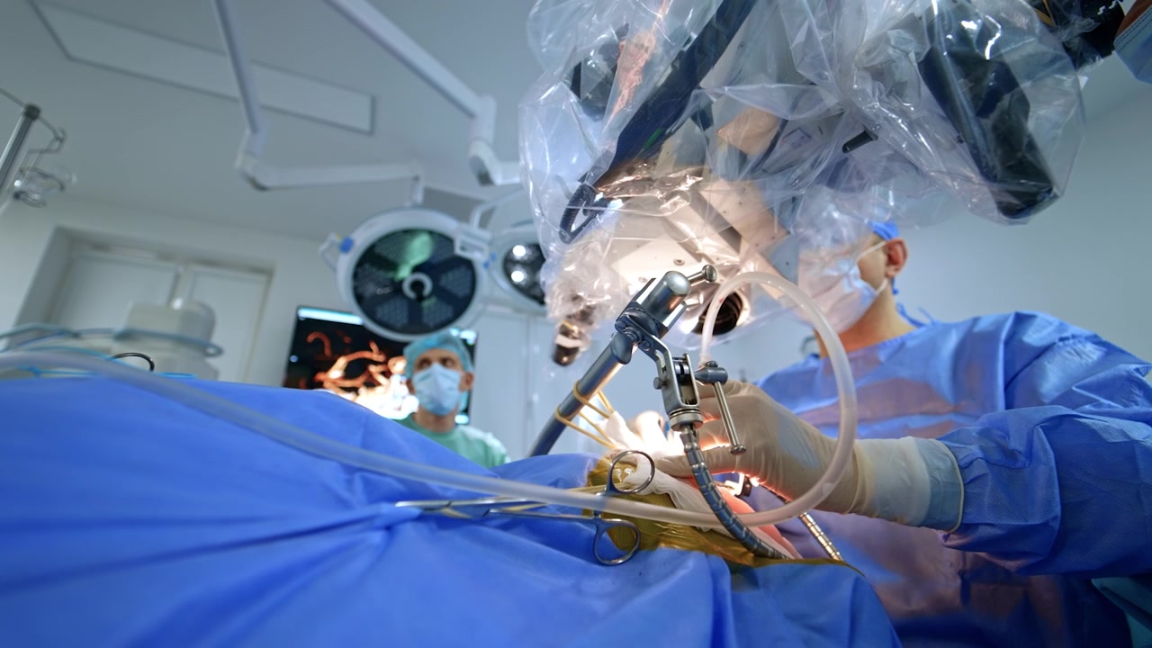 Unrecognized male surgeon uses instruments looking at microscope. Low angle view at the doctor performing neurosurgery.
