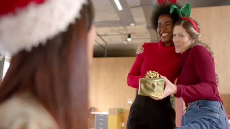 happy diverse female creative colleagues giving christmas presents in office, slow motion