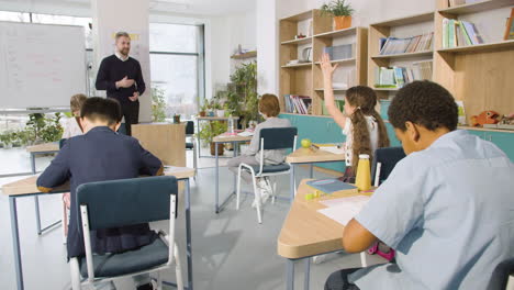 male english teacher explaining past simple to primary pupils on the whiteboard in classroom at school