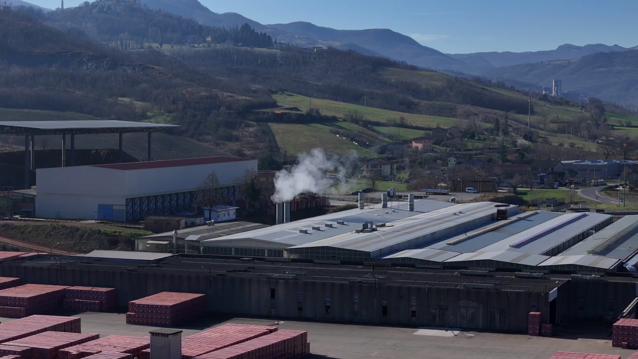 Fábrica de tijolos com produtos de argila vermelha, grandes pavilhões de produção e uma chaminé alta de forno ocupa o Vale do Arda perto de Lugagnano Val d'Arda, Piacenza, Itália, sobrevoo frontal de drone