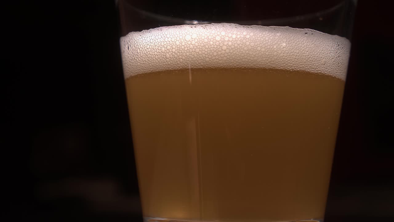 burbujas carbonatadas forman una cabeza sobre un vaso de cerveza rubia pálida.