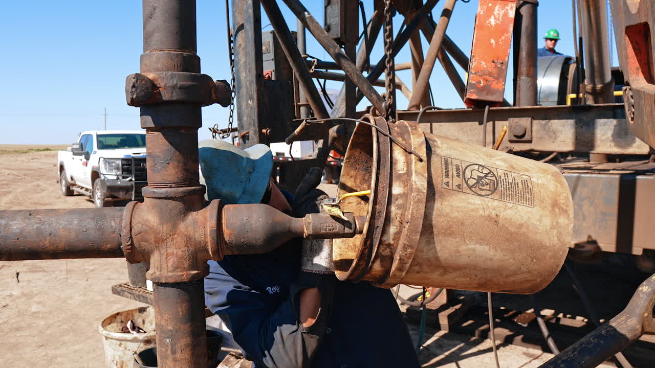 Man holding a bucket at the pipe filling it. Location for drilling oil in the desert.