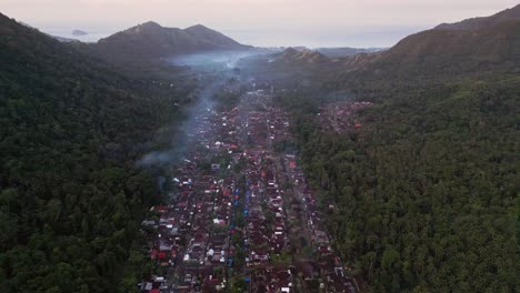 Drone footage captures an ancient town in Indonesia nestled in a rural valley, showcasing historical architecture with traditional wooden houses and thatched roofs surrounded by natural landscape