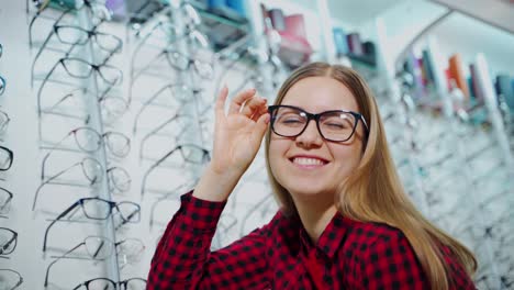 smiling girl buying eyeglasses in the shop. attractive young woman trying on new glasses and posing on camera at optics store.