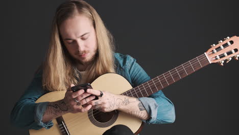 joven caucásico con guitarra usando su teléfono inteligente en la cámara.