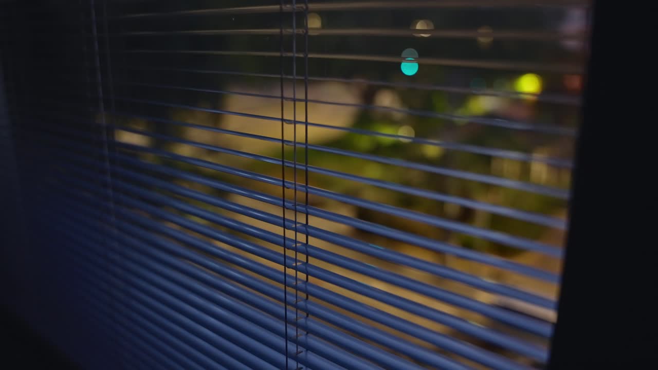 Close up on window shutters or blinds at night overlooking quiet city street. Suspicious person point of view pov shot. Hidden spying or searching for something outside. Secret operation or hideout