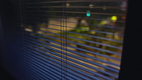 close up on window shutters or blinds at night overlooking quiet city street. suspicious person point of view pov shot. hidden spying or searching for something outside. secret operation or hideout