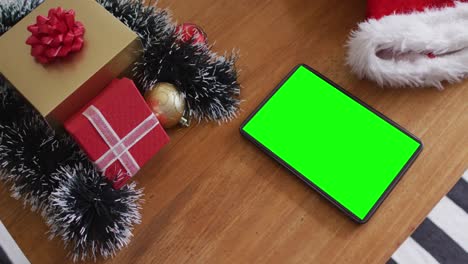 Tablet-Mit-Grünem-Bildschirm-Auf-Dem-Tisch-Mit-Weihnachtsmützen-Und-Weihnachtsgeschenken