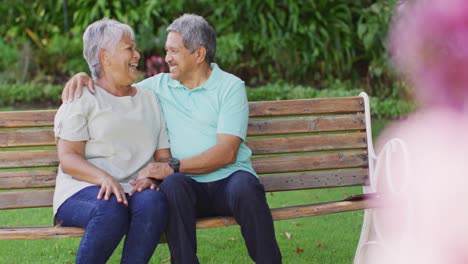 Video-Eines-Glücklichen-Gemischtrassigen-älteren-Paares,-Das-Sich-Umarmt-Und-Auf-Einer-Bank-Im-Garten-Sitzt