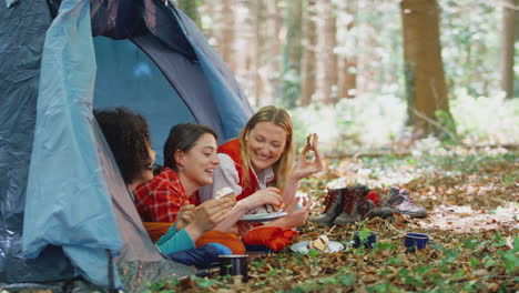 group of female friends on camping holiday in forest lying in tent eating s'mores