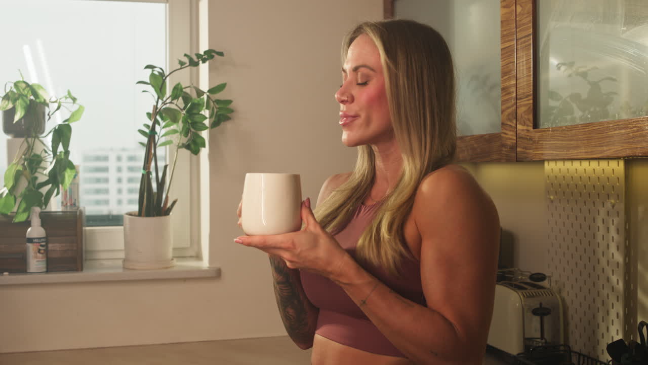 Fit woman enjoys hot drink in cozy kitchen morning light calm self care routine at home, self care soothing