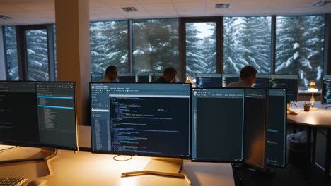 programmers working in a tech office with multiple monitors and a snowy forest view