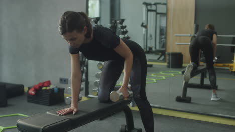 woman performing a dumbbell row exercise in a gym