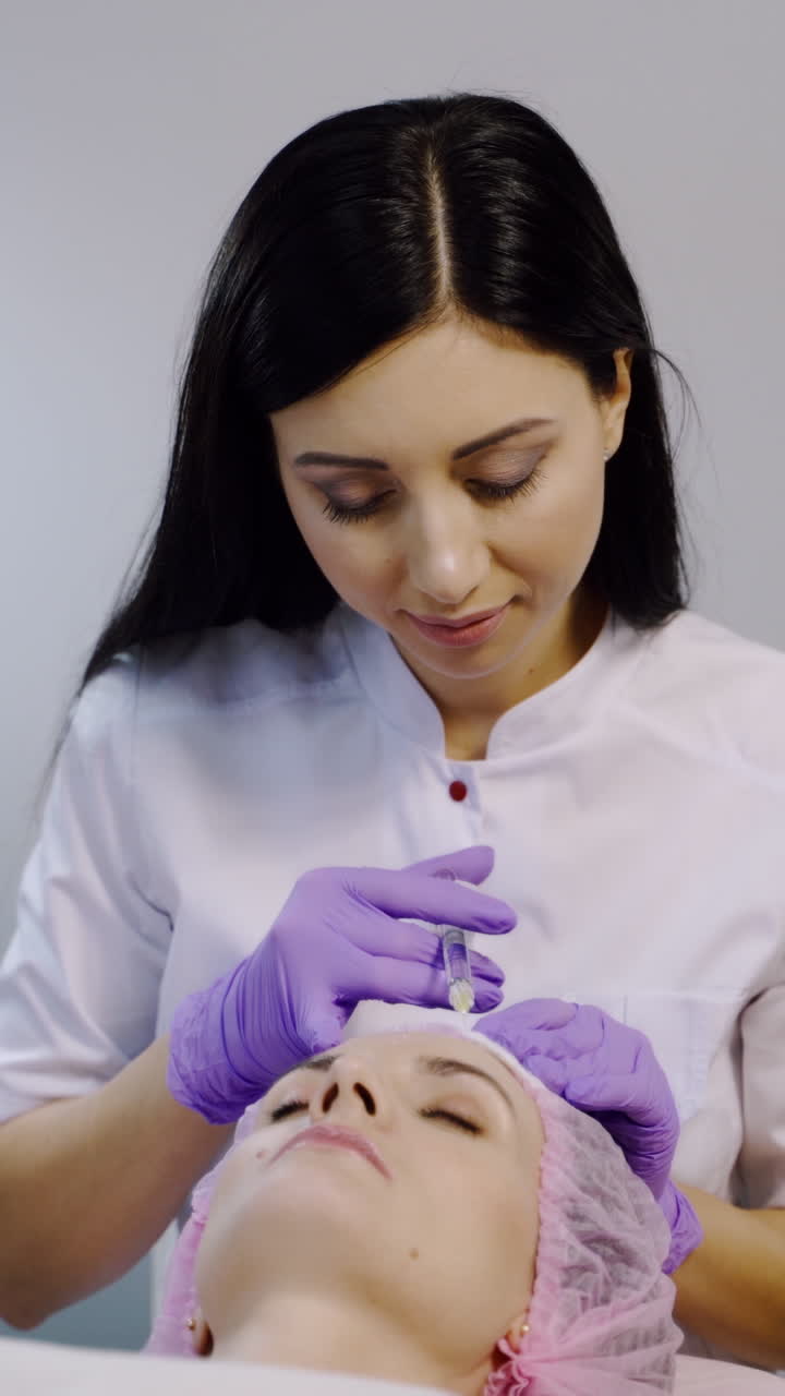 A woman on the procedure of injections in a cosmetology clinic. Preventing wrinkles. Vertical video