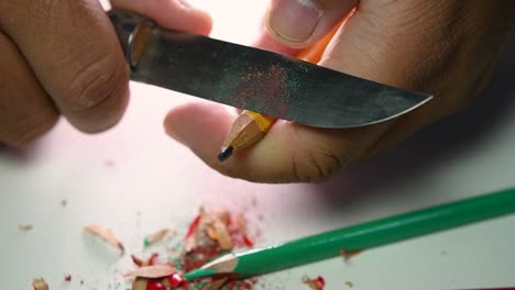 imágenes de manos afilando lentamente un lápiz y algunos lápices de colores con un cuchillo afilado