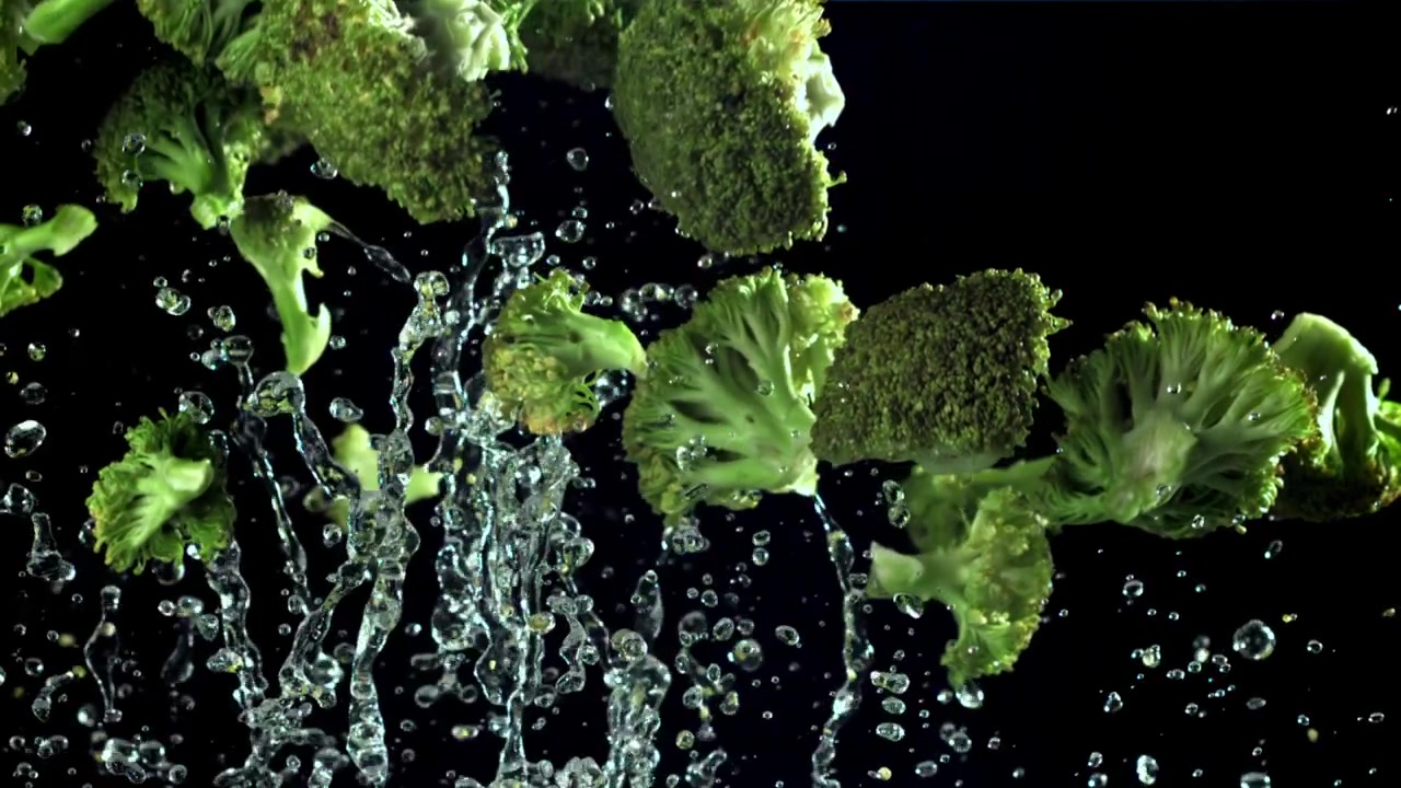 Cimette di broccoli fresche che cadono con schizzi d'acqua al rallentatore