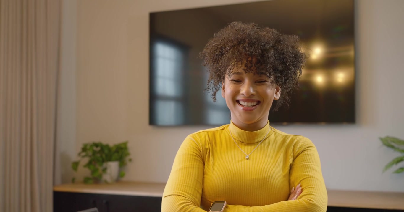 Donna afroamericana che tiene una tazza, scorre il telefono dopo un avviso, rivolta verso la fotocamera in ufficio con un laptop.