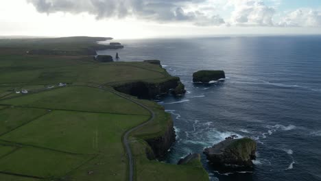 aerial view of kilkee cliffs in ireland with lush greenery and a meandering road at dusk