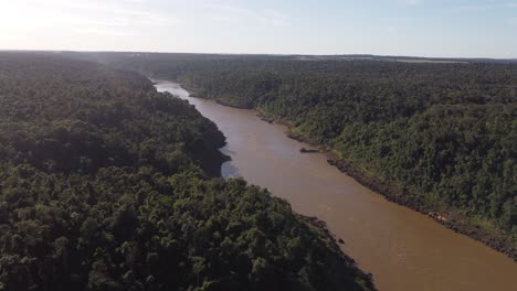 aerial view of flowing dirty brown colored iguazu river in middle of amazon rainforest at sunlight