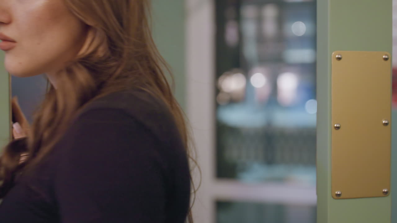 Lady walking toward entrance while reaching to open transparent glass door, reflections visible on surface, interior signage and light background detail creating depth and context to indoor movement