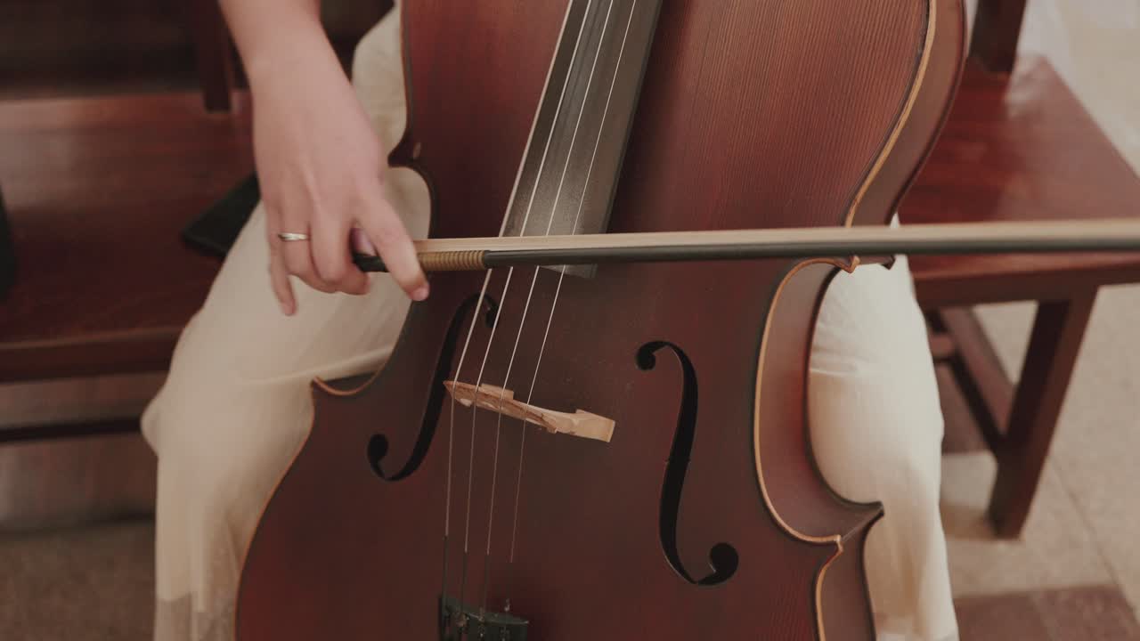 close up of a hand playing cello with bow inside a softly lit indoor space