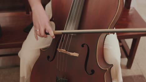 close up of a hand playing cello with bow inside a softly lit indoor space
