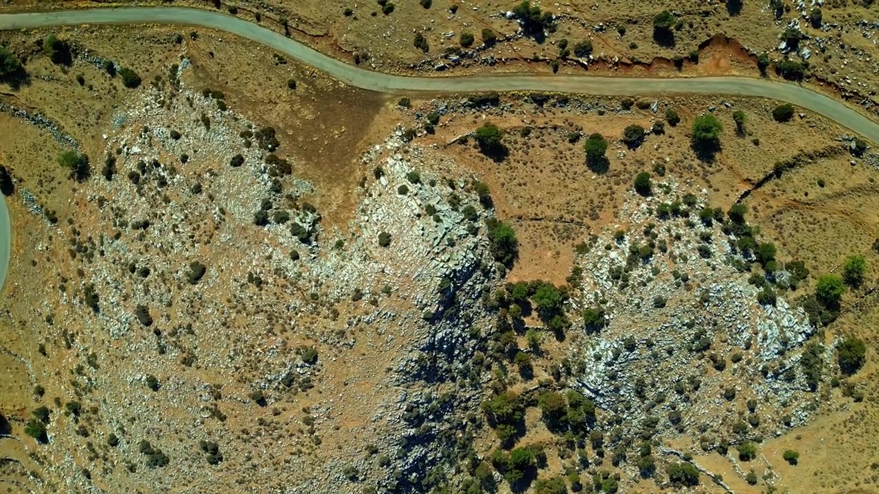 Arbusti sparsi e affioramenti rocciosi pallidi coprono le aride colline di Katafigio Agrias Zois Trigiodo mentre un sentiero tortuoso si snoda attraverso il terreno arido