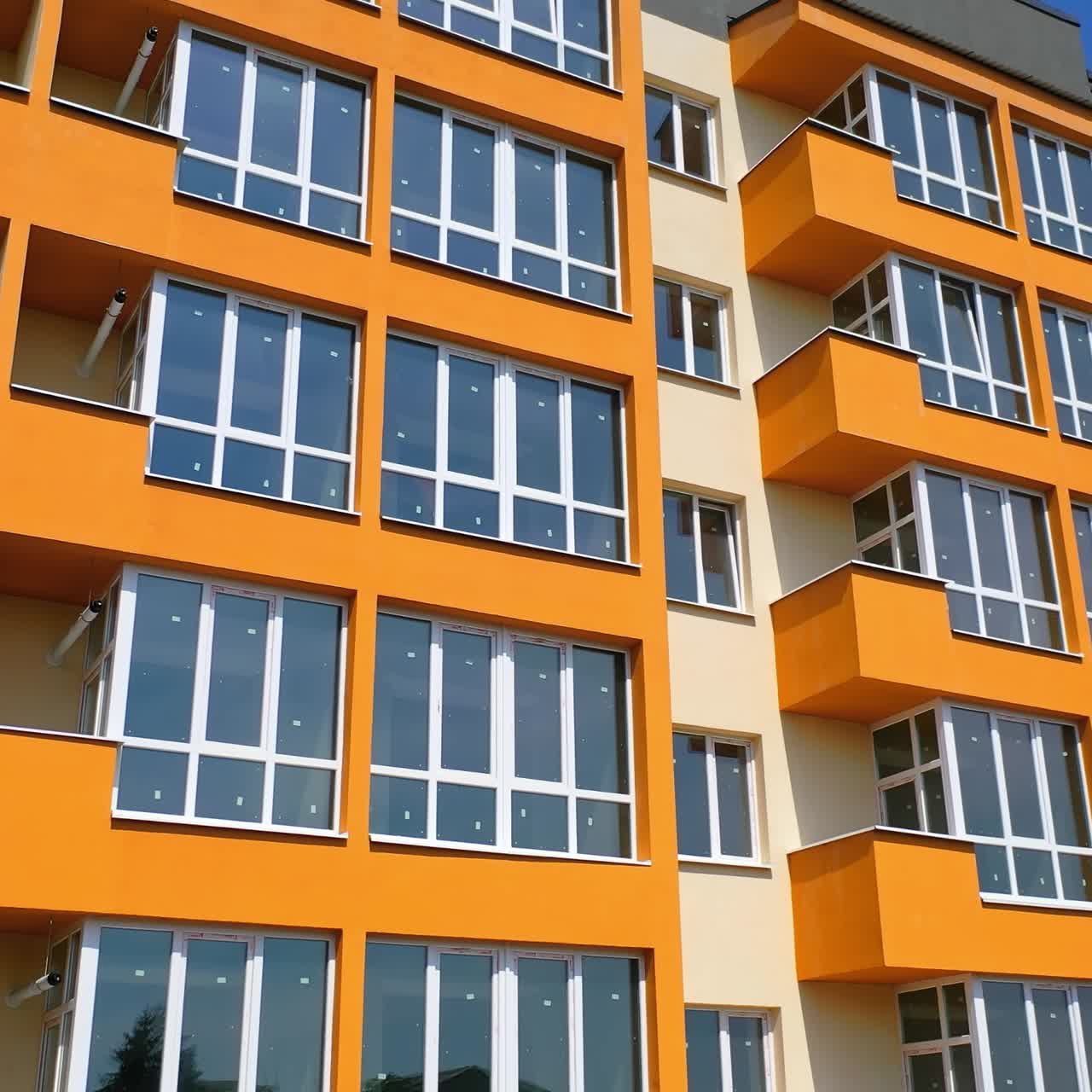 Modern high rise building with glazed balconies. Front view of newly built block of flats with colorful walls. New apartment building facade in the city