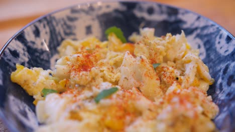 vista de cerca de huevos revueltos con paprika y perejil en un tazón azul sobre una mesa de cocina