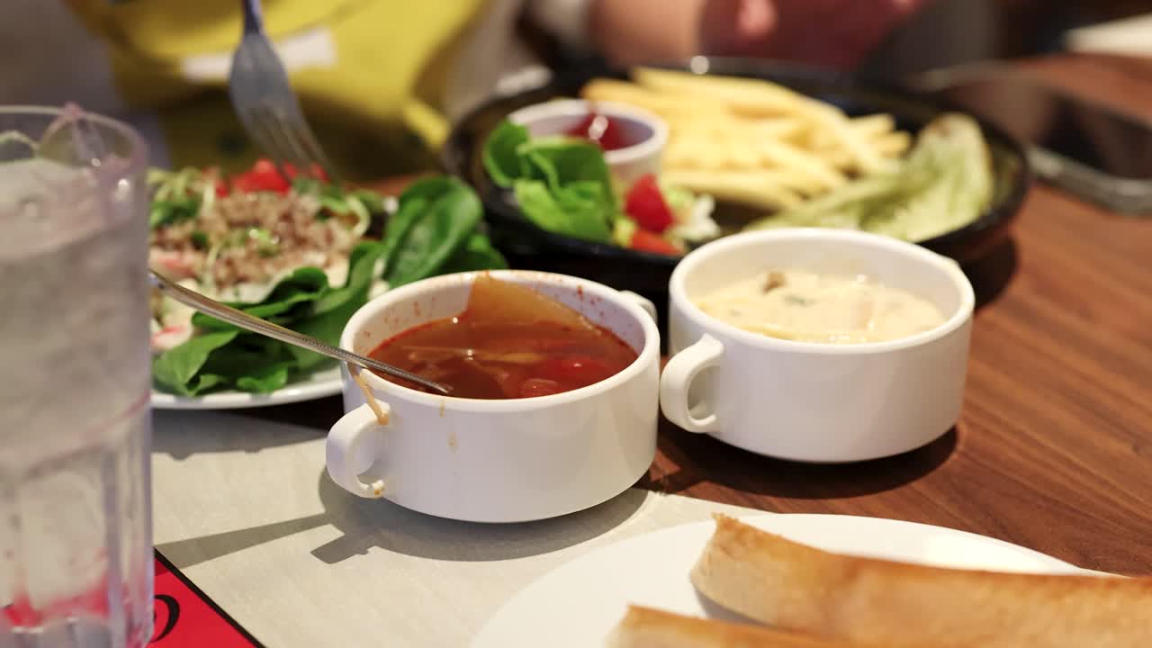 Diner enjoys buffet with red soup, creamy soup, salad, fries, and bread under bright lighting