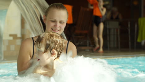 Mutter-Hält-Sohn,-Der-Im-Rauen-Wasser-Des-Pools-Planscht