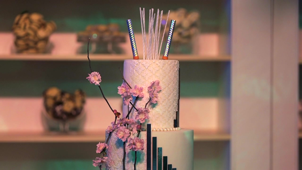 Una torta splendidamente realizzata, adornata con fiori rosa e stelline luminose, si erge elegantemente su uno sfondo delicatamente illuminato. Adatta per immagini di pianificazione eventi o promozioni di celebrazioni