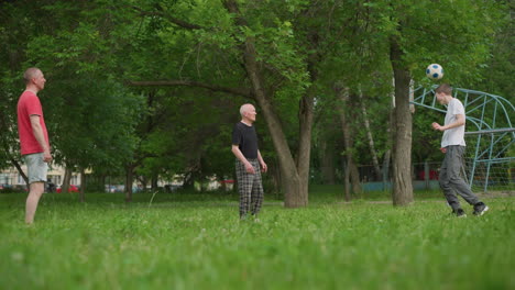 a family moment where a son heads away a soccer ball passed to him by his father, aiming it towards his grandfather in a grassy field