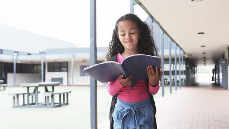 in a school corridor, a young biracial girl is engrossed in reading a book