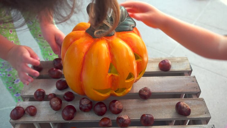 Little girl playing feeding chestnuts to halloween pumpkin, child play, holiday decoration, unrecognizable