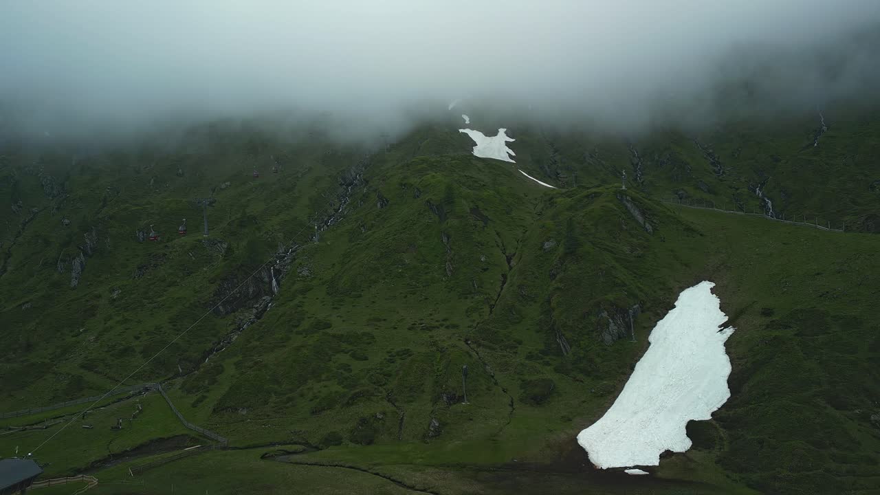 Grønne fjell med røde gondoler som går inn og ut av skyene
