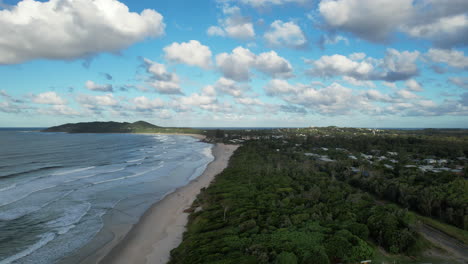 byron bay coastline with waves, greenery, and distant mountains under a vibrant sky, aerial view