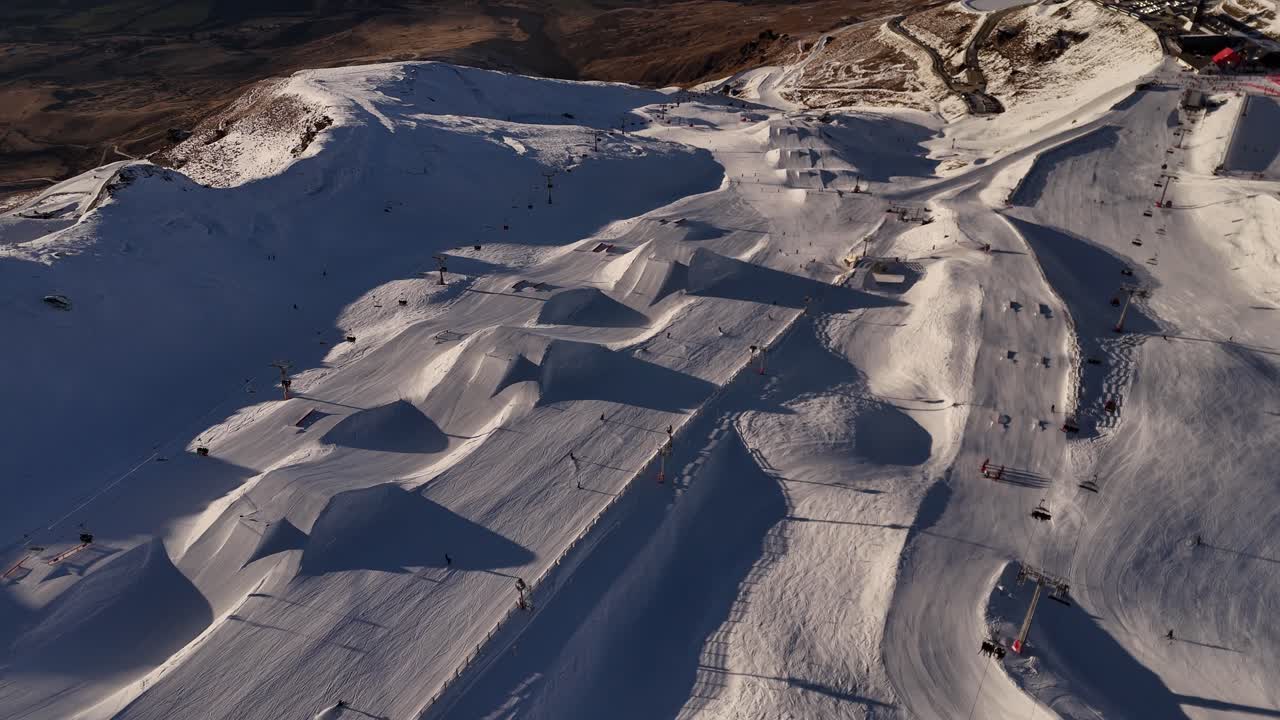 Vista aerea dall’alto di persone che sciano sulle pendici innevate delle montagne di Cardrona in Nuova Zelanda. Alba dorata al mattino