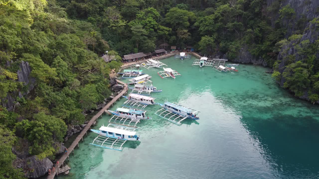 Touristen auf einem Holzsteg am Anlegesteg für Ausflugsboote des Kayangan-Sees auf Coron Island.