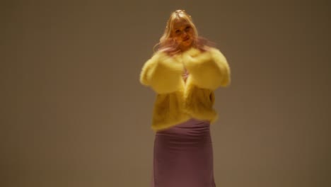 mujer rubia con abrigo de piel amarillo y camiseta púrpura