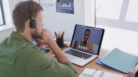 Caucasian-man-using-laptop-and-phone-headset-on-video-call-with-male-colleague